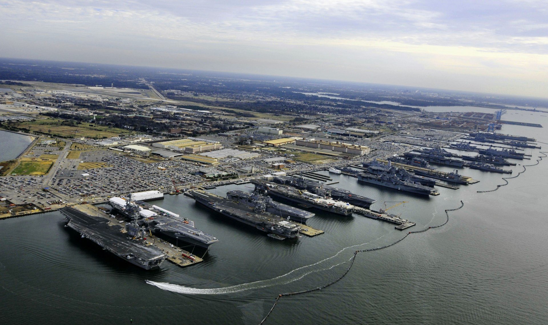 Aerial view of a naval base featuring multiple aircraft carriers docked in the water, with a sprawling landscape of land and sea in a high-definition desktop wallpaper.