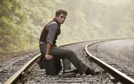 A striking HD wallpaper featuring Robert Pattinson in a scene from Water for Elephants, seated on a railway track amidst a misty forest backdrop.