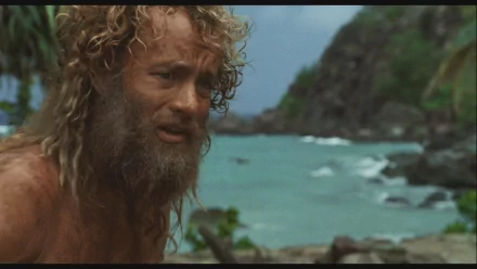 HD PC desktop wallpaper: bearded castaway on a rocky tropical shore, waves and cliffs behind him — scene from the movie Cast Away.