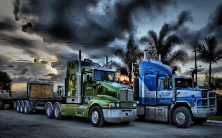 Two trucks, one green and one blue, are parked side by side under a dramatic sky with palm trees in the background. This high-definition image serves as a desktop wallpaper and background.