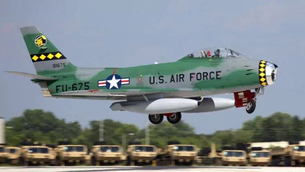 A U.S. Air Force aircraft in flight, showcasing a vibrant green and yellow design, with military vehicles visible in the background. This HD desktop wallpaper emphasizes aviation and military themes.