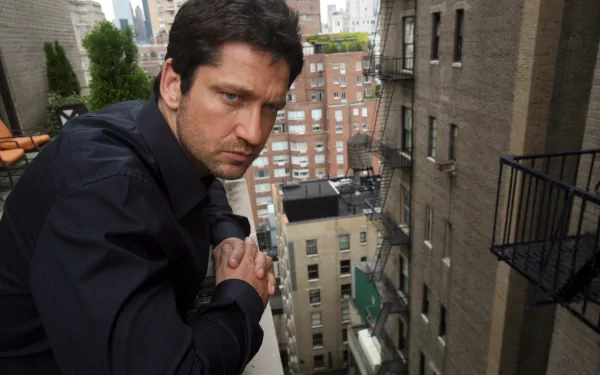 A captivating HD desktop wallpaper featuring celebrity Gerard Butler leaning on a ledge, with a cityscape of buildings in the background.