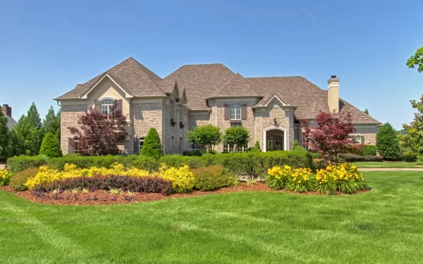 A charming man-made house surrounded by vibrant gardens and lush greenery, providing a serene backdrop for an HD PC desktop wallpaper. Bright blue sky enhances the picturesque scene.