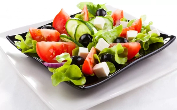 HD PC desktop wallpaper featuring a fresh salad with lettuce, tomato wedges, cucumber slices, black olives, and cubes of white cheese on a black plate.