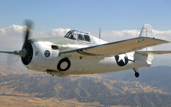 HD desktop wallpaper featuring a Grumman F4F Wildcat military aircraft flying over a mountainous landscape under a blue sky.