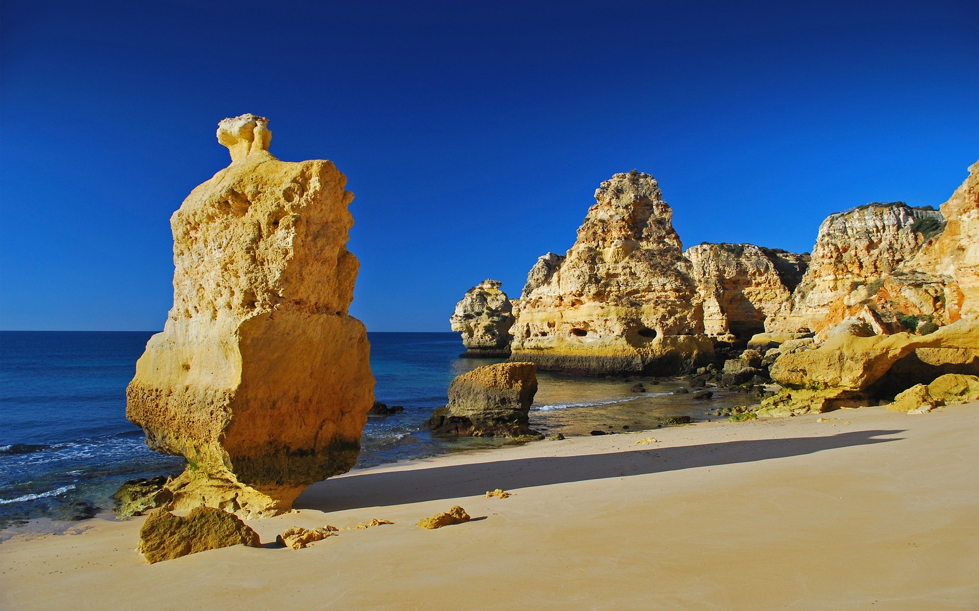 HD PC desktop wallpaper showcasing a pristine beach with towering nature-carved cliffs under a clear blue sky.