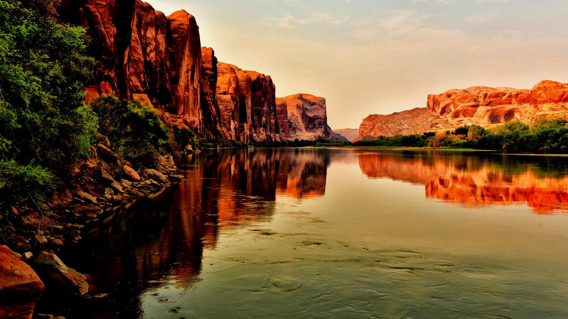 HD PC desktop wallpaper of nature and reflection: red canyon cliffs and greenery mirrored in a calm river beneath a warm, glowing sky.