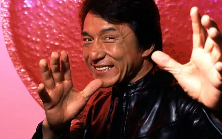 High-definition desktop wallpaper featuring Jackie Chan posing with a playful smile against a vibrant pink background.