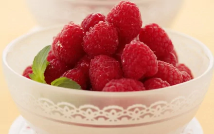 A close-up HD desktop wallpaper of fresh raspberries in a white decorative bowl with a mint leaf garnish.