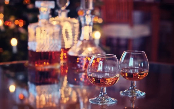 HD PC desktop wallpaper featuring two whisky glasses and decanters on a reflective surface, highlighting rich amber tones in a cozy, dimly lit setting with food ambiance.