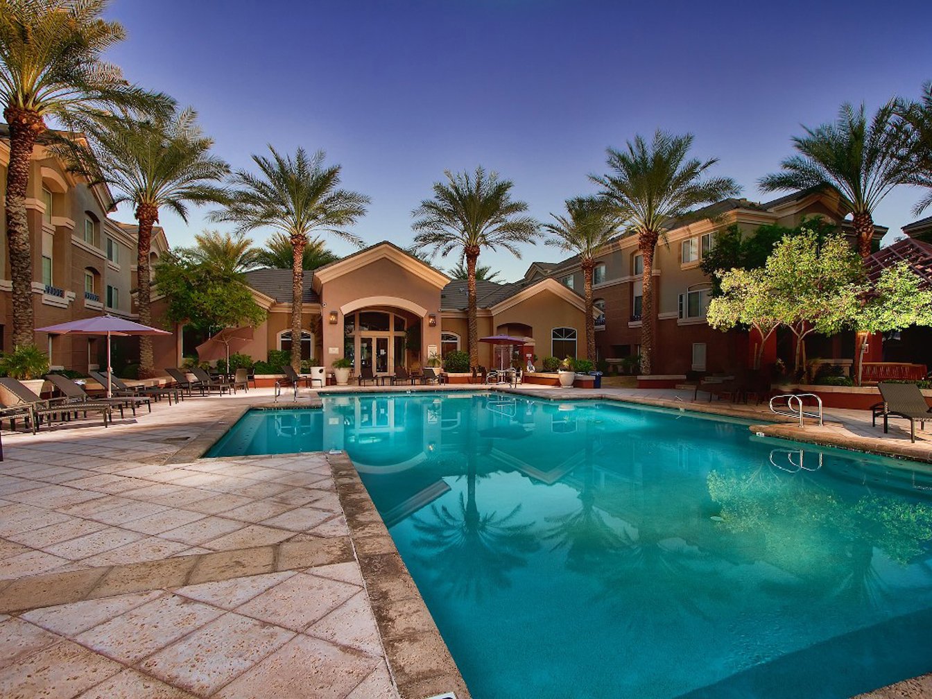 HD PC desktop wallpaper and background: man-made pool courtyard with palm trees, lounge chairs, and Mediterranean-style buildings at dusk.