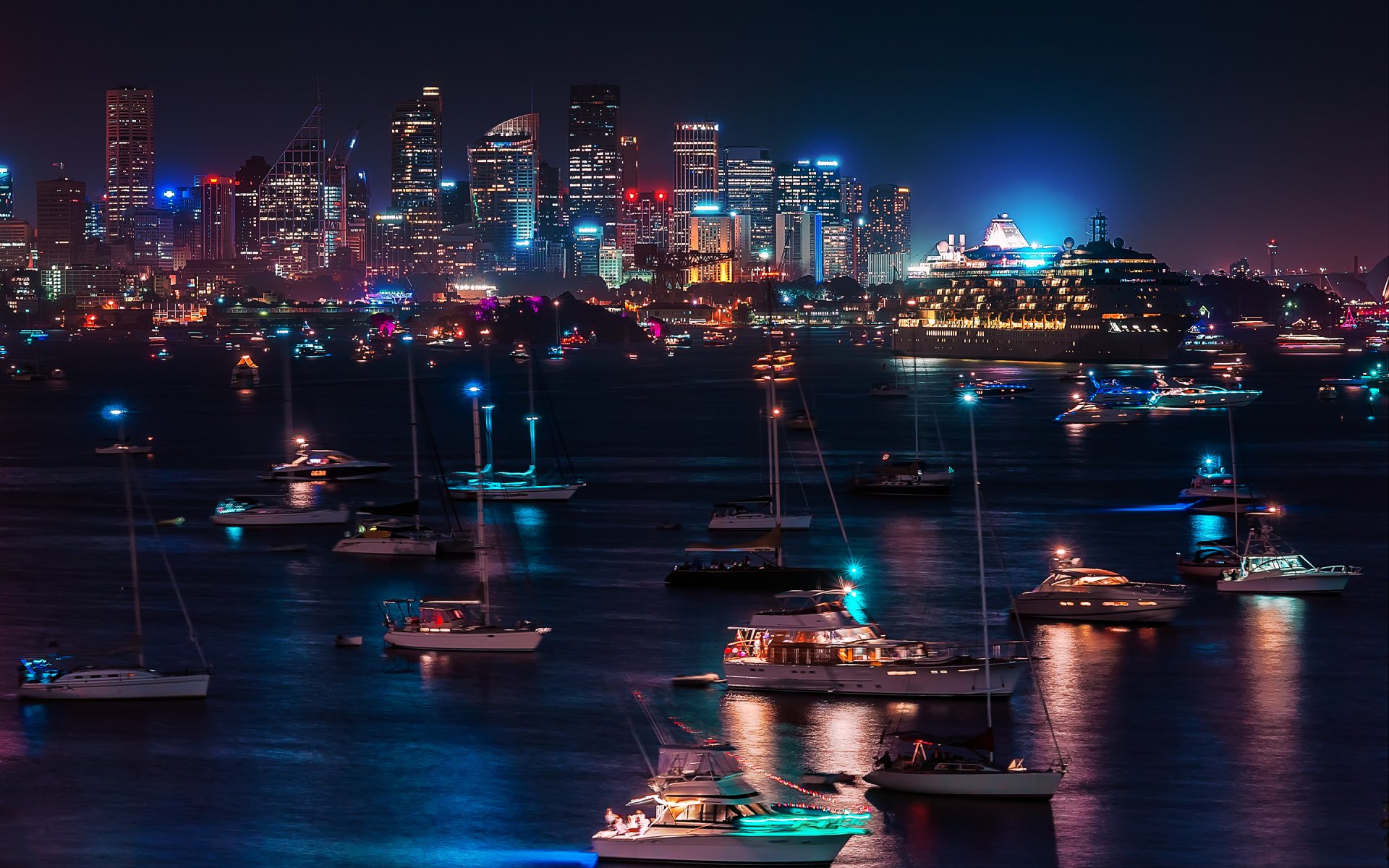 Sydney, Australia night skyline with the Opera House and moored boats glowing across the harbor, vibrant city lights — 2K Quad HD PC desktop wallpaper/background