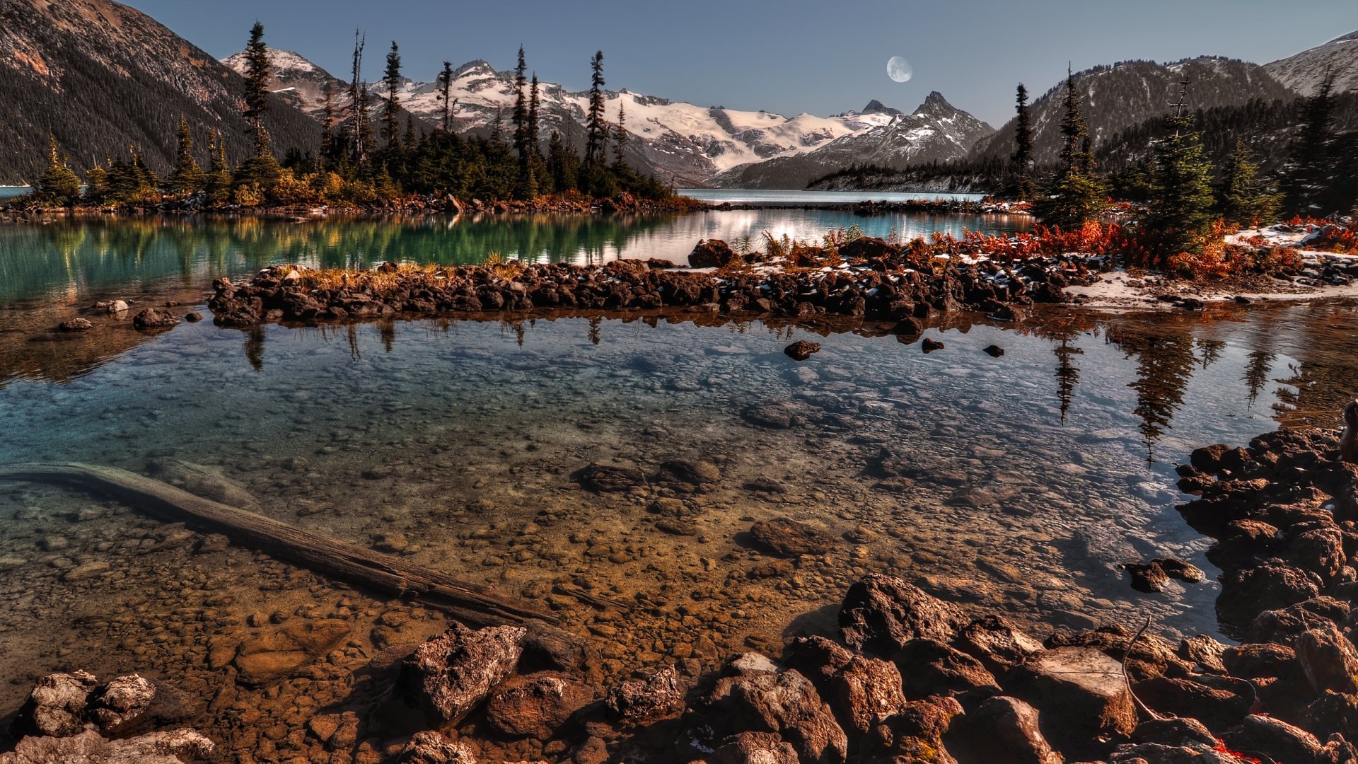 HD PC desktop wallpaper showcasing a serene mountain lake surrounded by snow-capped peaks and autumnal trees under a clear sky with a visible moon.
