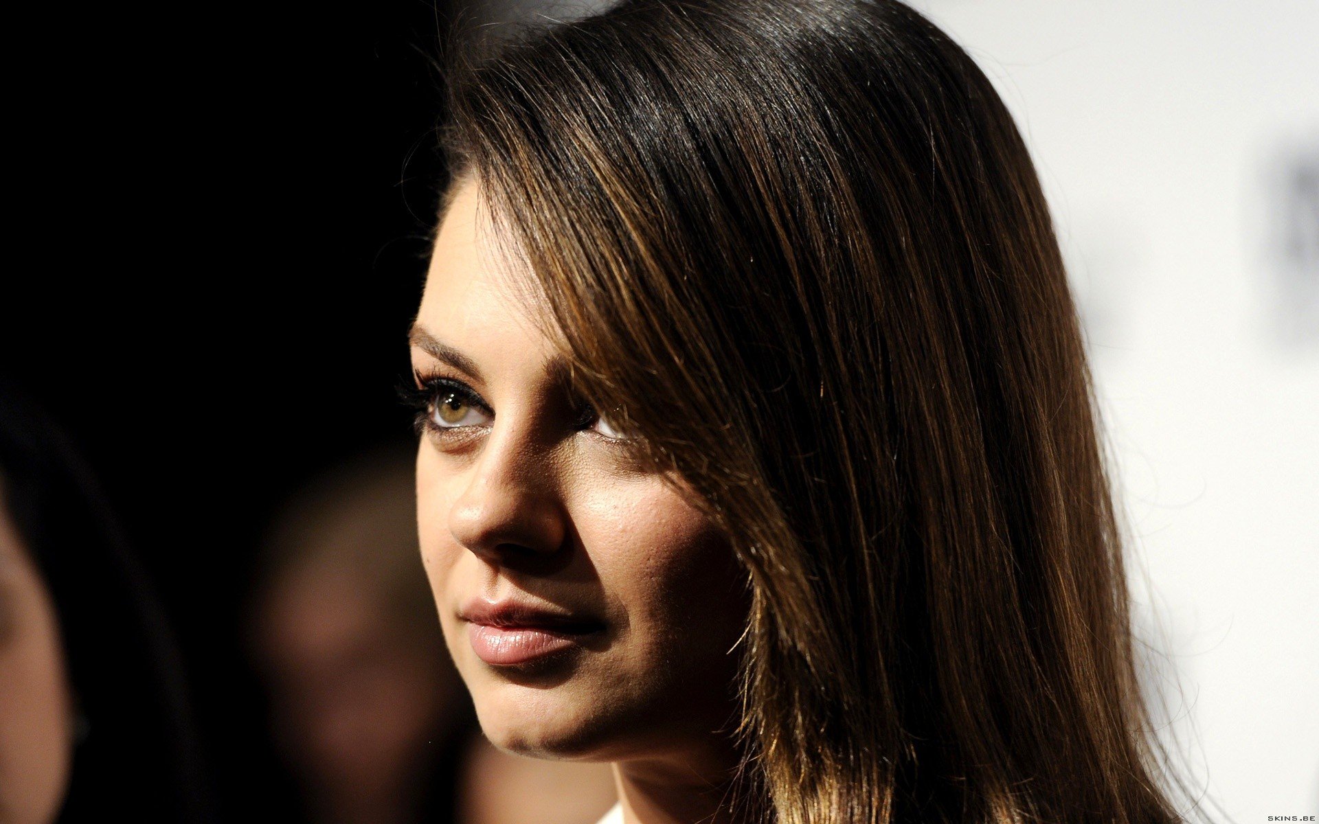 HD PC desktop wallpaper featuring a close-up portrait of celebrity Mila Kunis with soft lighting highlighting her face against a dark background.