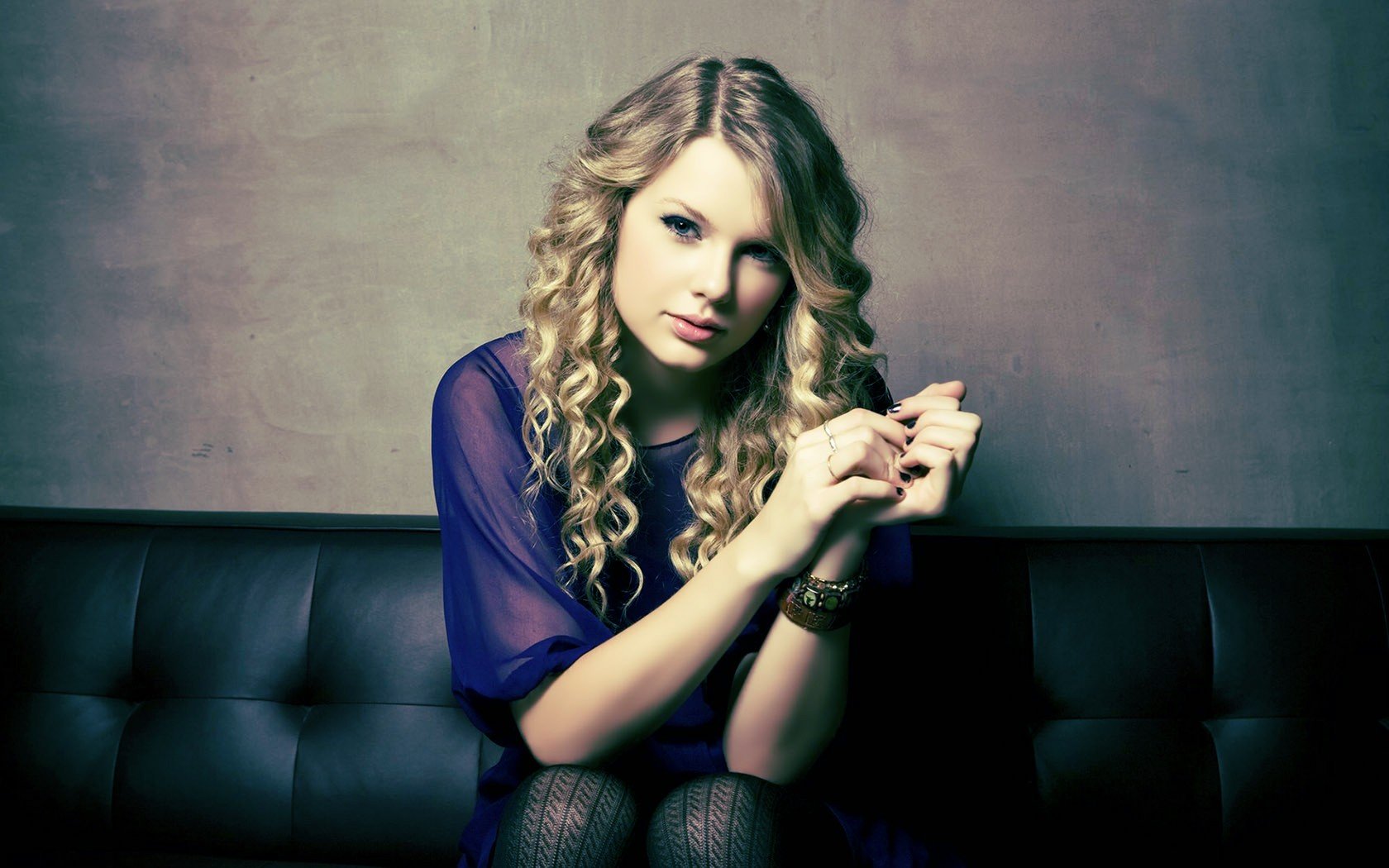 HD PC desktop wallpaper featuring Taylor Swift with curly hair, wearing a dark outfit, set against a muted gray background, representing music and style.
