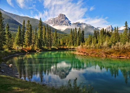 HD PC desktop wallpaper featuring a serene mountain landscape with pine trees reflected in a calm, turquoise lake under a partly cloudy sky.