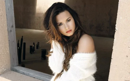Demi Lovato poses effortlessly in a cozy white sweater, framed by a rustic window. This HD wallpaper captures her striking beauty within a minimalist background.