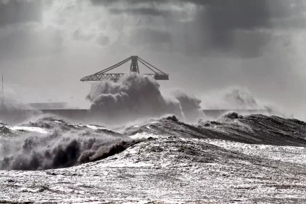 4K Ultra HD PC desktop wallpaper and background: dramatic nature storm — black-and-white seascape with towering waves crashing toward a distant industrial crane silhouette beneath heavy storm clouds.
