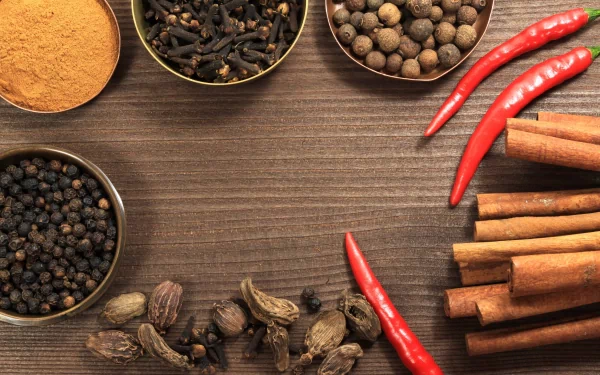 A 4K Ultra HD desktop wallpaper featuring an assortment of herbs and spices, including cinnamon sticks, red chili peppers, black peppercorns, and ground spice powders on a wooden surface.