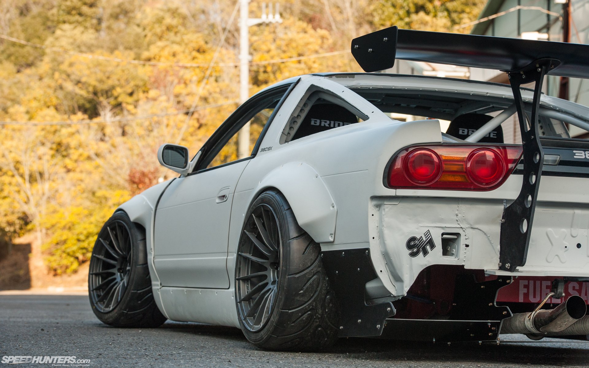 HD desktop wallpaper featuring a modified Nissan JDM vehicle with wide body fenders and a large rear wing, set against an autumn backdrop.