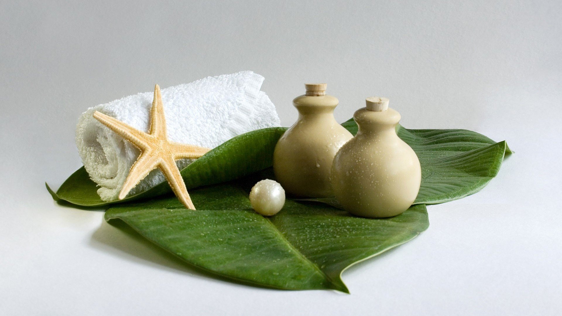 A serene still life featuring a white towel, natural elements, and spa accessories atop green leaves, creating a tranquil atmosphere for relaxation.
