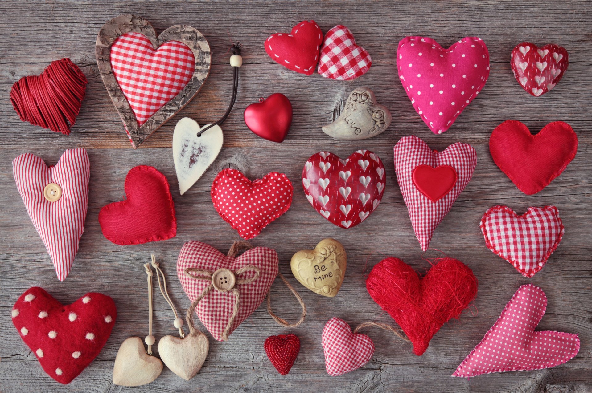 A vibrant collection of artistic hearts in various textures and patterns, featuring shades of red and pink, displayed against a rustic wooden background. 4K Ultra HD desktop wallpaper.