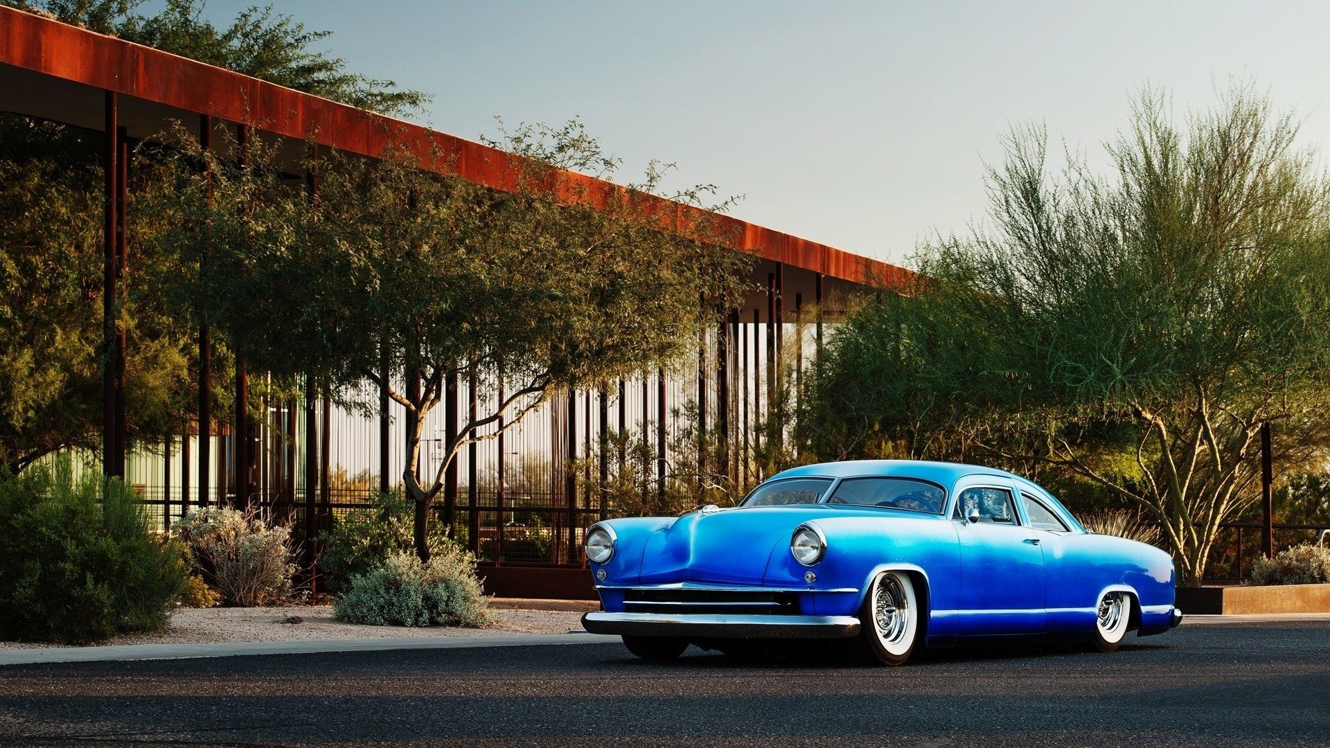 Blue 1951 Kaiser Dragon Coupe vehicle parked beside desert shrubs under a modern canopy - HD PC desktop wallpaper/background.