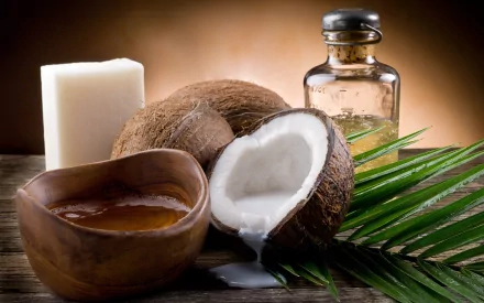 An HD desktop wallpaper featuring coconuts, coconut oil, and soap, arranged with a green palm leaf on a wooden surface, creating an inviting and natural aesthetic.