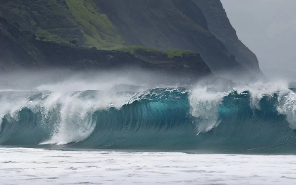 HD desktop wallpaper showcasing a powerful ocean wave crashing near a rocky, green mountainside under a misty sky, highlighting the beauty of nature.