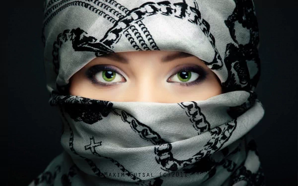 HD wallpaper of a woman wearing a patterned scarf, revealing only her vivid green eyes and a hint of her face, exuding depth and mystique. The scarf and her hijab frame her expressive eyes beautifully.