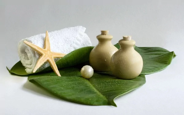 A serene still life featuring a white towel, natural elements, and spa accessories atop green leaves, creating a tranquil atmosphere for relaxation.