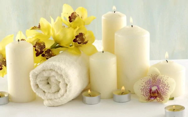 Still life HD wallpaper featuring yellow orchids, lit white candles, and a rolled white towel creating a serene spa atmosphere.