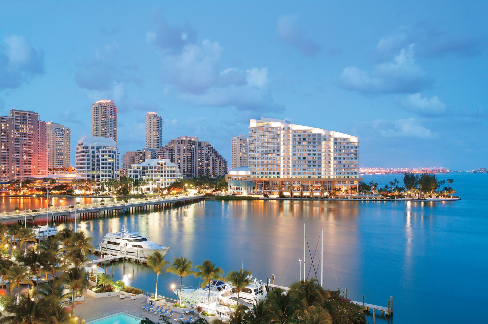 HD desktop wallpaper of Miami, Florida waterfront skyline at dusk — illuminated man-made high-rises, palm-fringed marina and calm bay reflecting city lights.