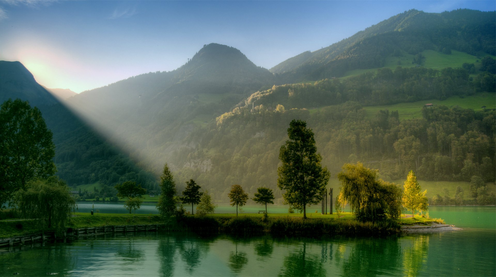 4K Ultra HD PC desktop wallpaper and background: serene nature scene with sunbeam slicing across a misty lake, tree‑lined island and rolling green hills.