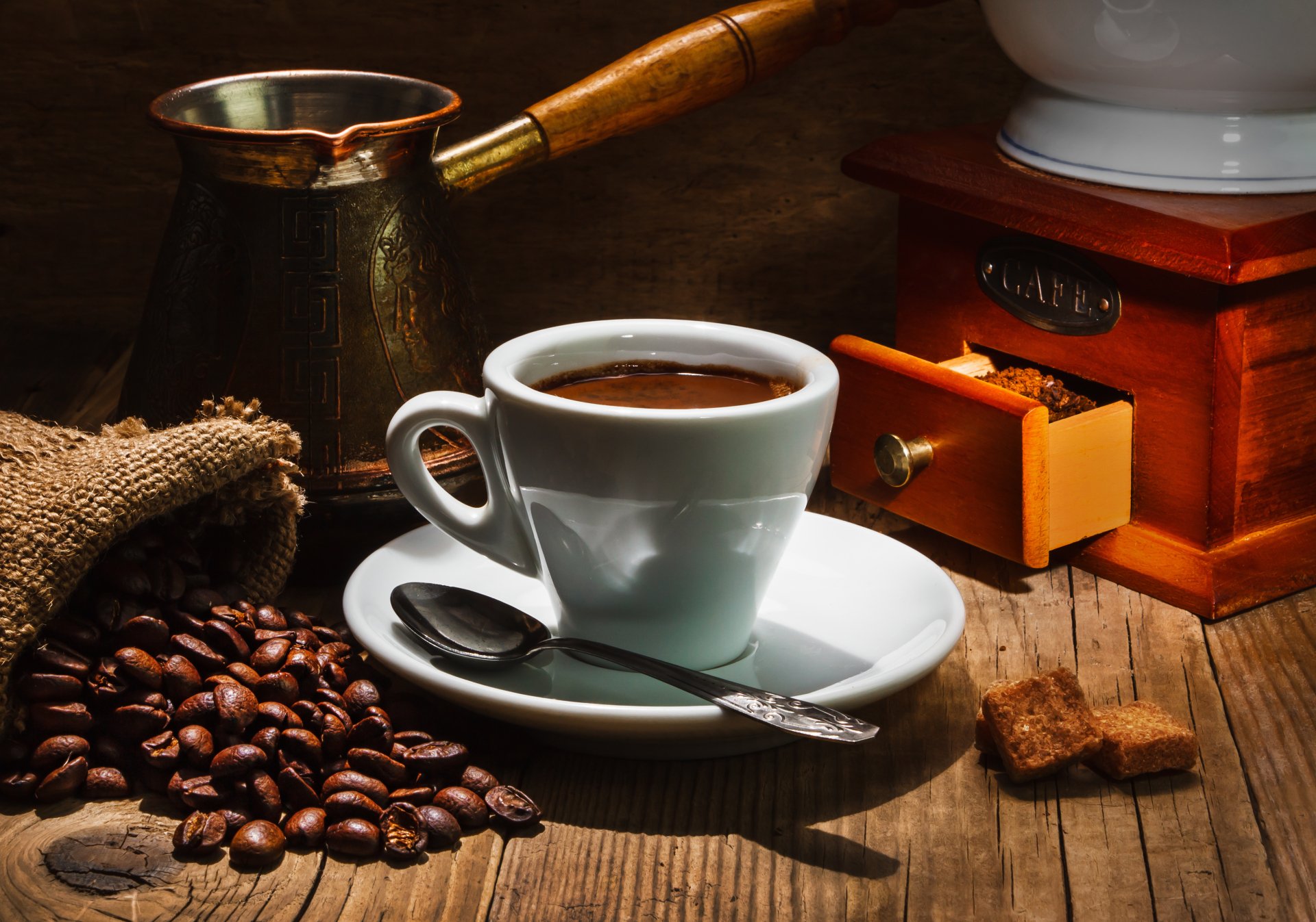 4K Ultra HD PC desktop wallpaper showing a cup of coffee with a spoon on a wooden table, surrounded by coffee beans, a coffee grinder, and a cezve.