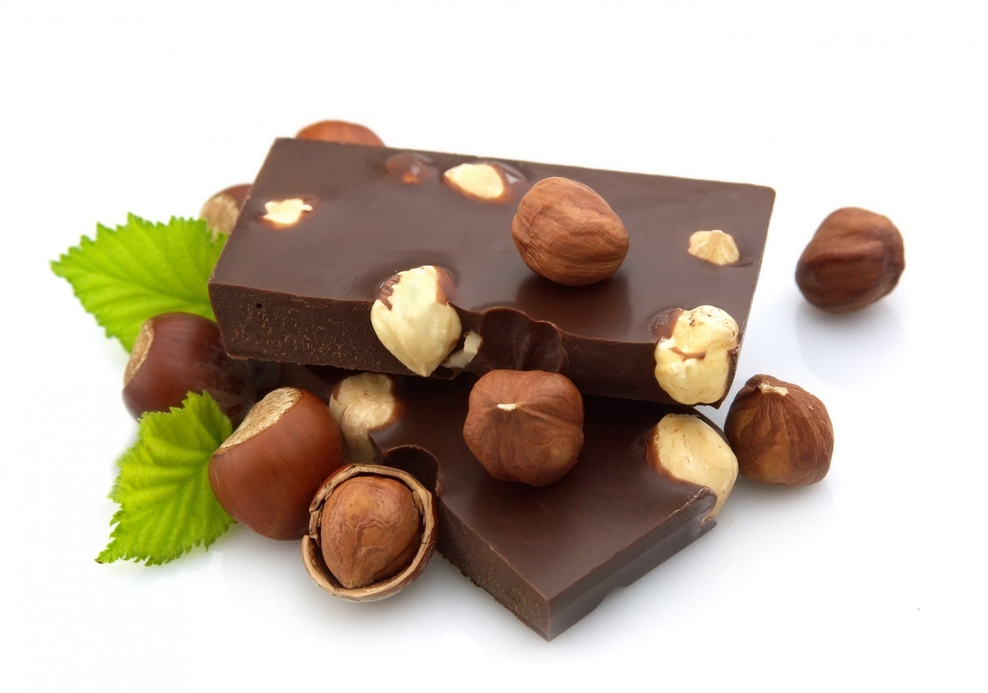 Delicious dark chocolate bars adorned with whole hazelnuts, complemented by fresh green leaves, create a tempting food-themed HD PC desktop wallpaper.