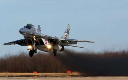A Mikoyan MiG-29 military jet takes off, producing a trail of smoke against a clear sky, showcased as a high-definition desktop wallpaper.