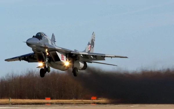 A Mikoyan MiG-29 military jet takes off, producing a trail of smoke against a clear sky, showcased as a high-definition desktop wallpaper.
