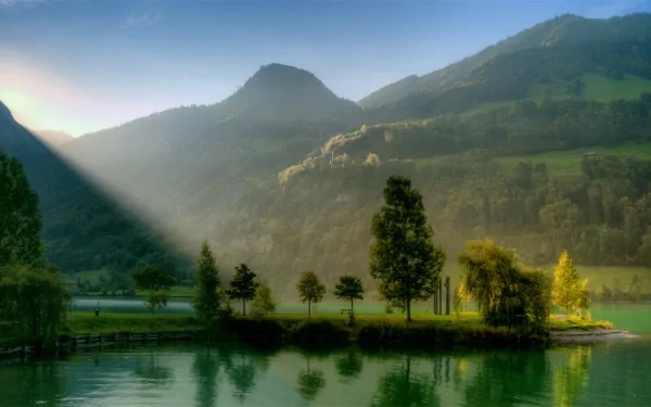 4K Ultra HD PC desktop wallpaper and background: serene nature scene with sunbeam slicing across a misty lake, tree‑lined island and rolling green hills.