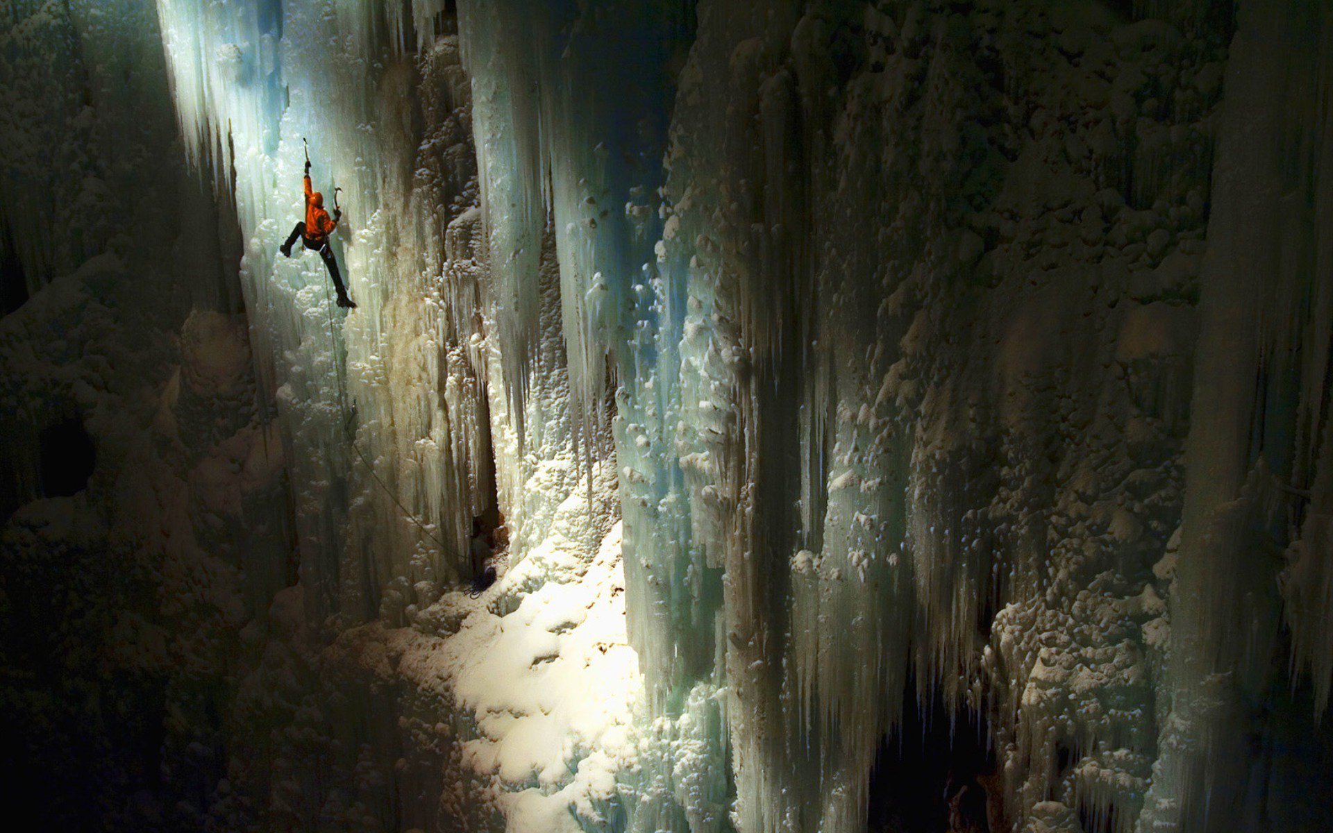 HD PC desktop wallpaper background — lone ice climber scaling a towering frozen waterfall by light, dramatic jagged ice textures, ice climbing sports action.