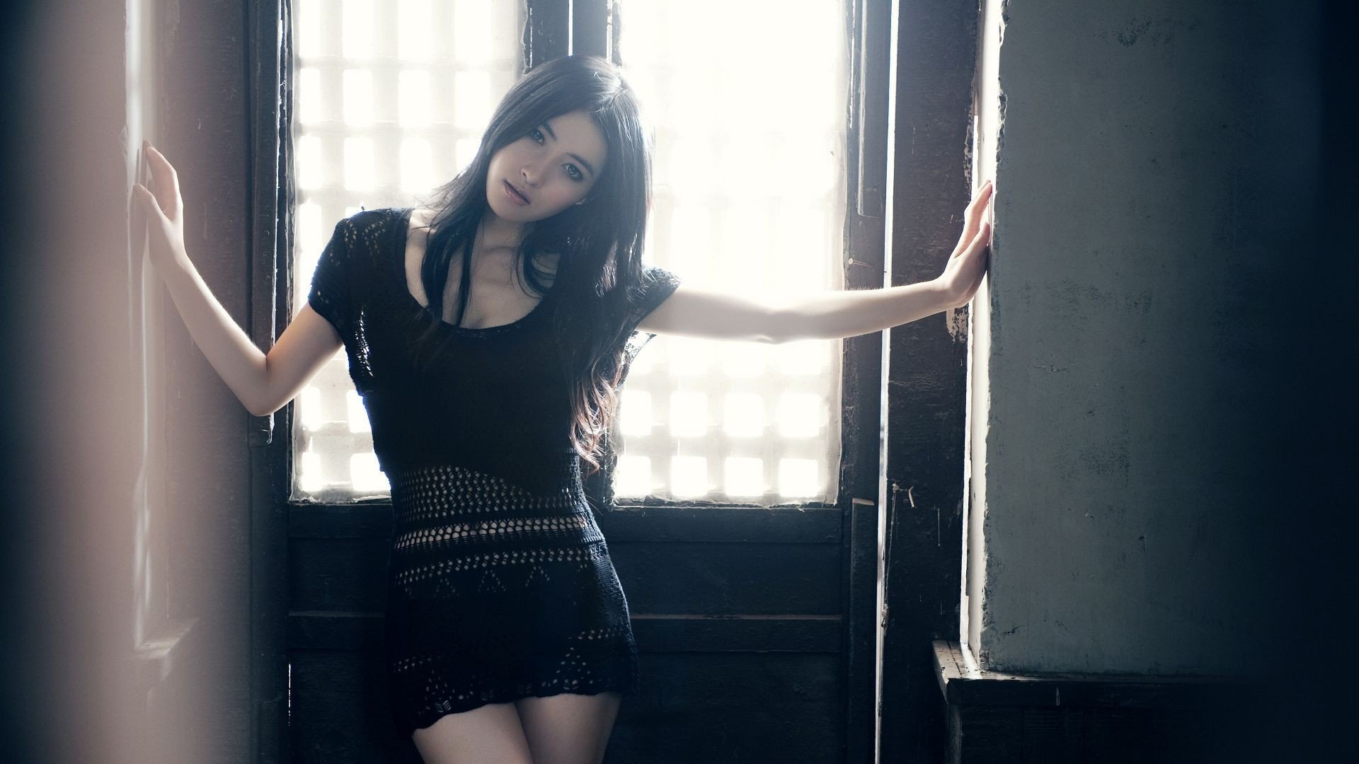 HD desktop wallpaper featuring a woman model in a black dress, standing by a softly lit window.