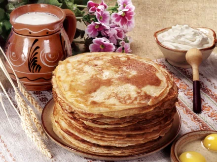 HD PC desktop wallpaper featuring a stack of golden crêpes accompanied by a rustic jug, bowl of cream, and pink flowers on a textured wooden surface.