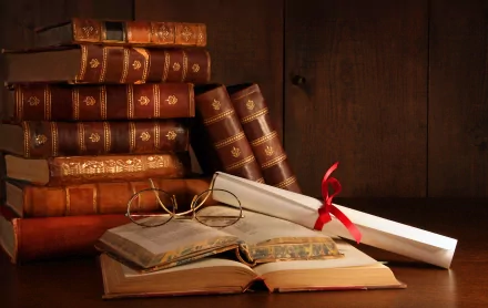 An HD desktop wallpaper featuring a stack of antique books, an open book with reading glasses, and a rolled scroll with a red ribbon on a wooden desk, set against a wooden background.