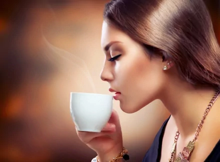 A woman with earrings and a necklace enjoys a cup of coffee, her face serene and profile illuminated. This HD desktop wallpaper captures the elegance and tranquility of the moment.