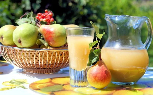 HD PC desktop wallpaper showing pear food: wicker basket of green pears, a red pear, and a glass and pitcher of pear juice on a sunlit table.