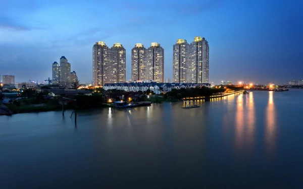 Man-made skyline of illuminated skyscrapers along a calm river at dusk — HD PC desktop wallpaper background.