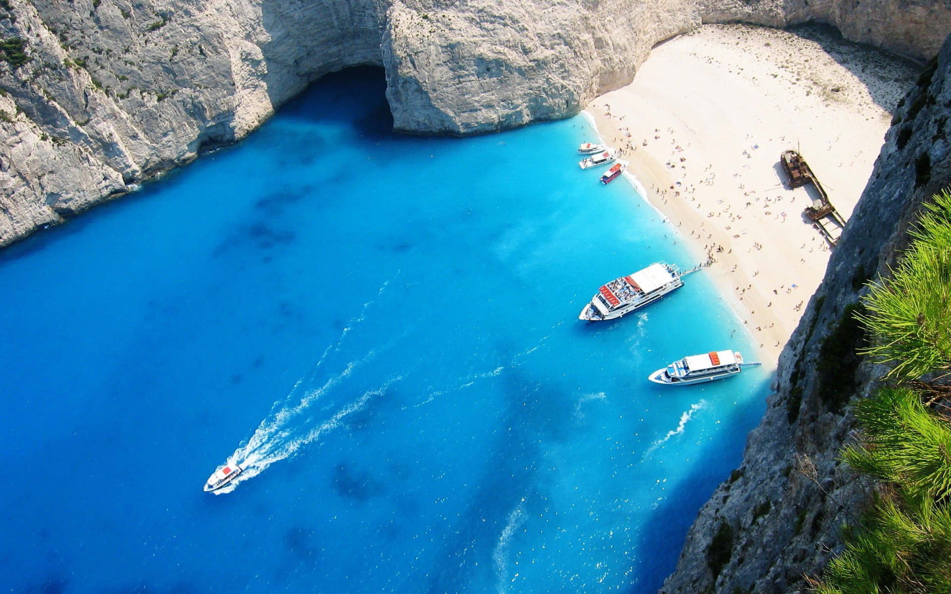 Aerial photography HD PC desktop wallpaper and background of a turquoise bay and white‑sand beach tucked in limestone cliffs, with small boats and a boat's wake.
