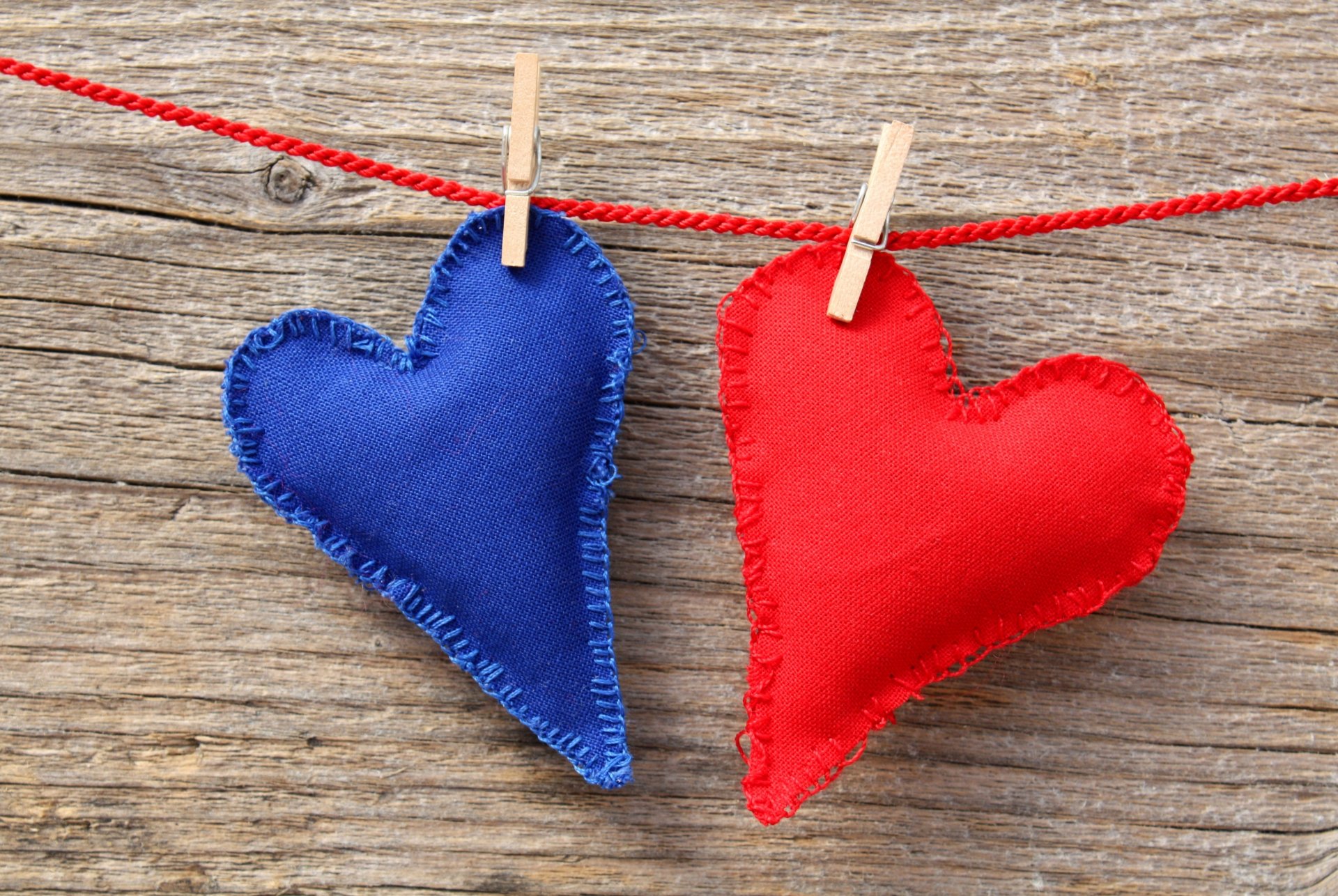 Artistic 4K Ultra HD wallpaper featuring blue and red fabric hearts hanging on a red string against a rustic wooden background.