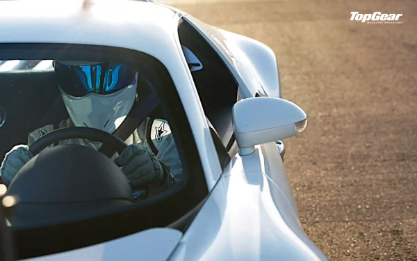 HD wallpaper of The Stig, from Top Gear, in full gear driving a car, with the Top Gear logo visible.
