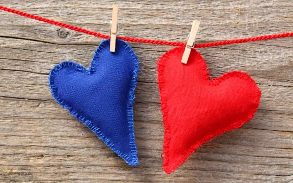 Artistic 4K Ultra HD wallpaper featuring blue and red fabric hearts hanging on a red string against a rustic wooden background.